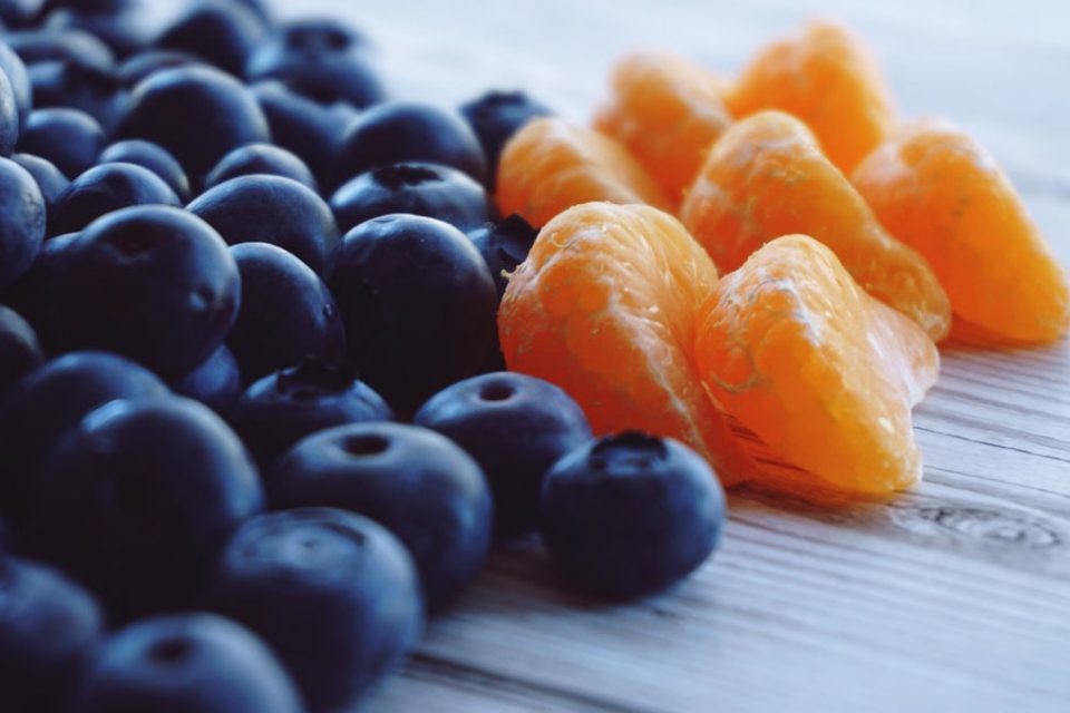 Close-up of fresh blueberries and tangerine segments arranged on a wooden surface, highlighting contrast and freshness.