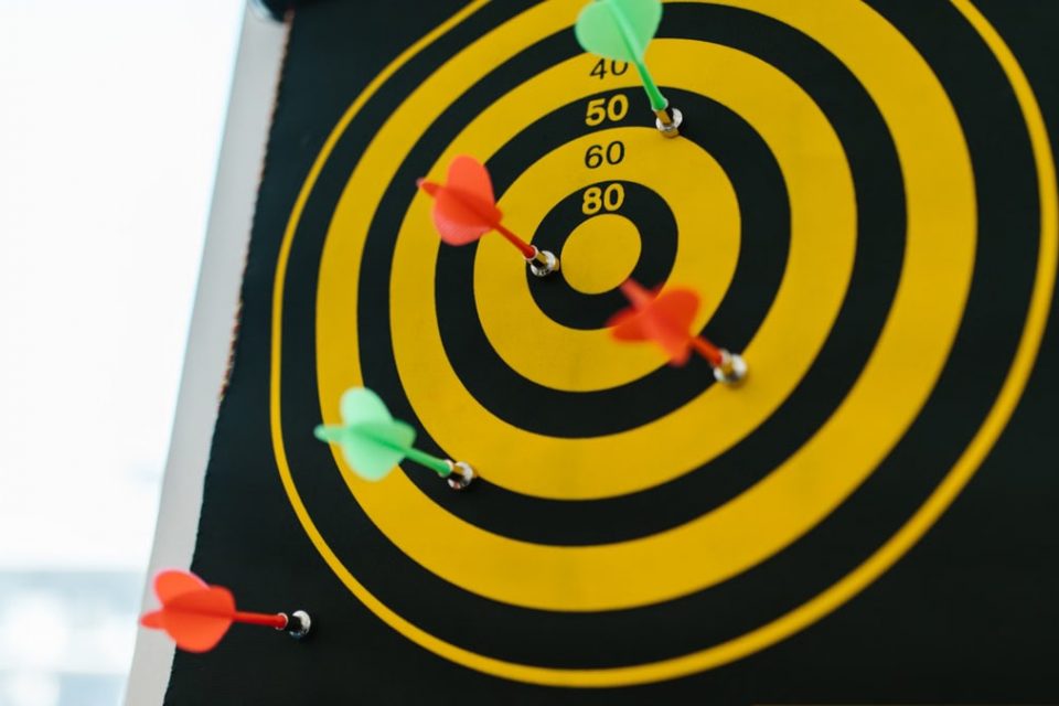 Vibrant darts stuck in a yellow and black dartboard representing precision and strategy.